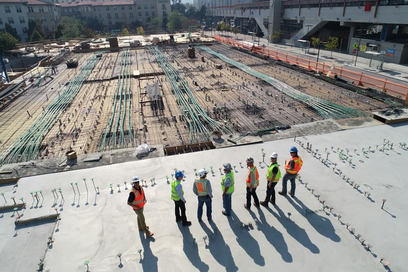 Construction crew in safety vests on the deck of a multi-story building under construction.