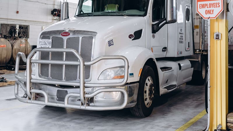 White heavy-duty semi truck parked inside a commercial repair shop service bay.