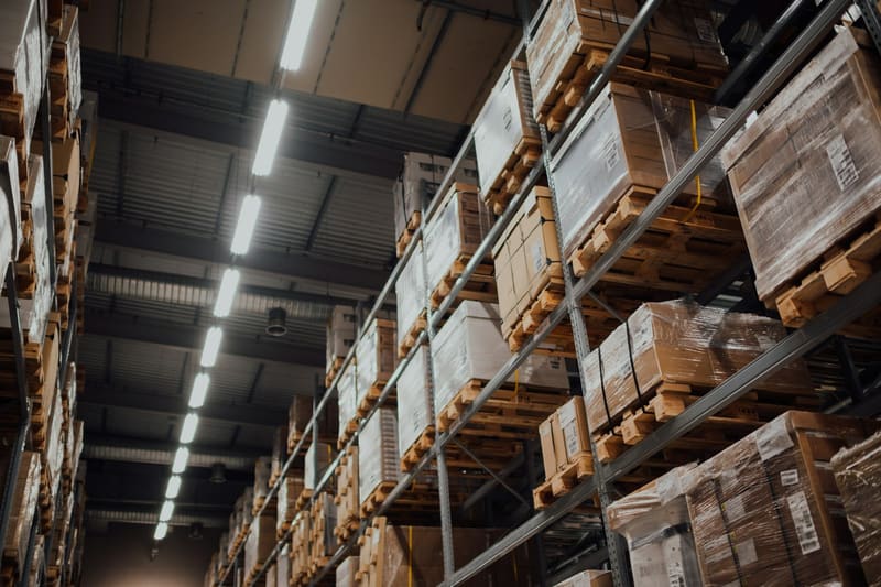 Industrial warehouse aisles lined with tall shelving stocked with palletized inventory.